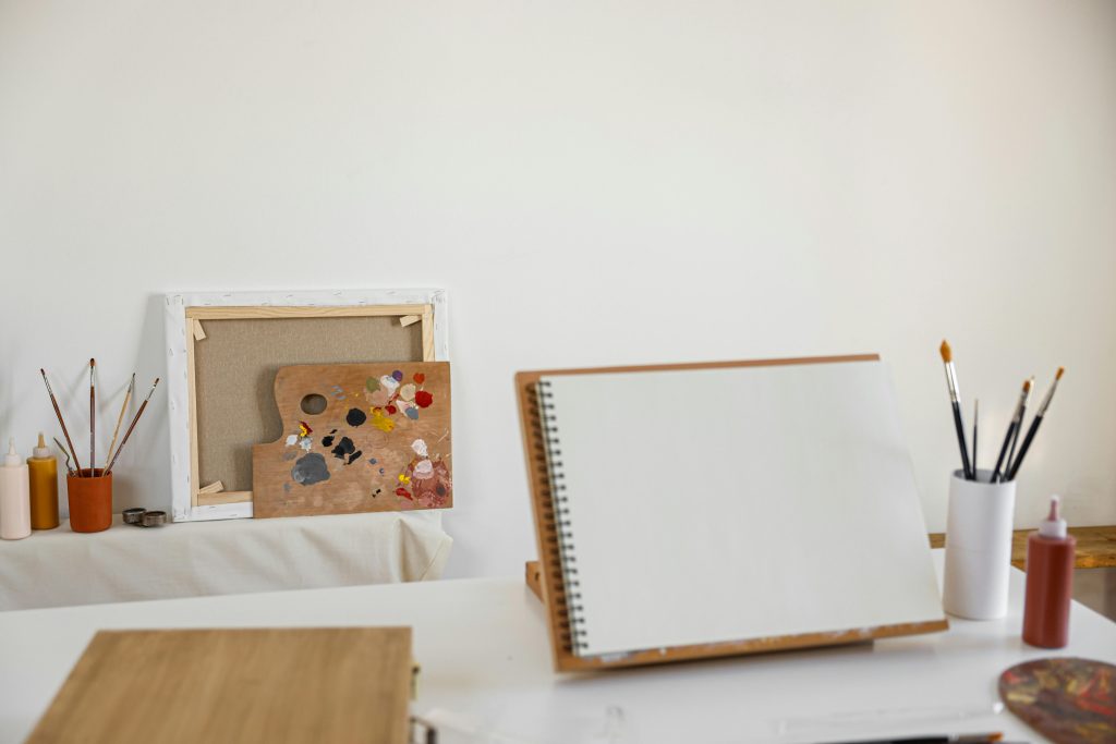 Cozy art studio setup with canvas, painting supplies, and blank notebook ready for creativity.